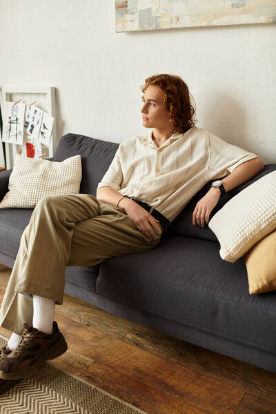 Young man comfortably seated on the couch, reflecting in his cozy home environment.