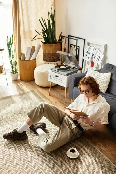 Evde dinlenen genç bir adam, rahat bir atmosferde kahvesini yudumlarken kitabın tadını çıkarıyor..