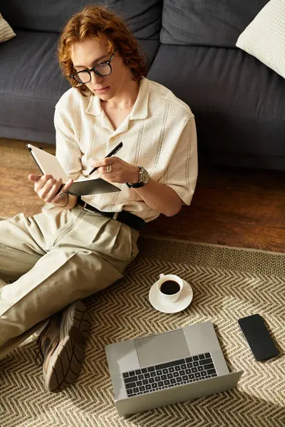 Rahatlamış genç adam evde yerde oturuyor, yanında kahve olan bir deftere yazıyor..