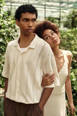 Genç çift yemyeşil bir serada kucaklaşıp gelişmekte olan bitkilerin arasında sevgilerini sergiliyor..