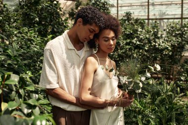 Sevgi dolu bir çift, yemyeşil bitkilerle çevrili seranın ortasında birbirine yakın durur..