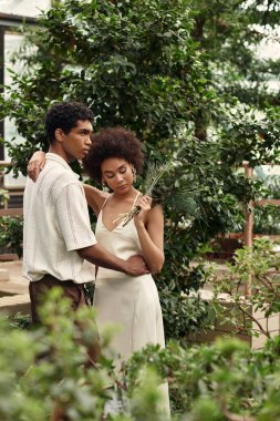 Huzurlu bir serada, genç bir çift canlı bitkiler arasında sarılır..