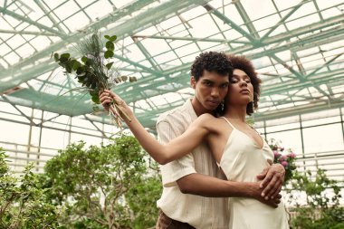 Sevgi dolu bir çift, canlı bitkilerin arasında tutkuyla sarılıp derin bağlantılarını vurgular..