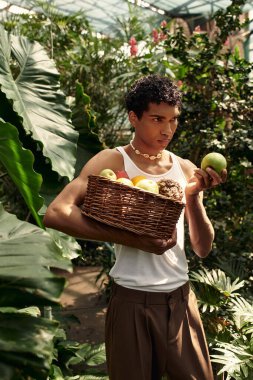 Genç ve şık bir adam yeşilliklerle çevrili zamanının tadını çıkarıyor, kendini ifade ediyor ve bitkilerin arasında gülüyor..