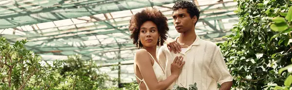 Genç bir çift, yemyeşil bitkilerle çevrili bir serada kucaklaşıp derin bağlarını ifade ederler..