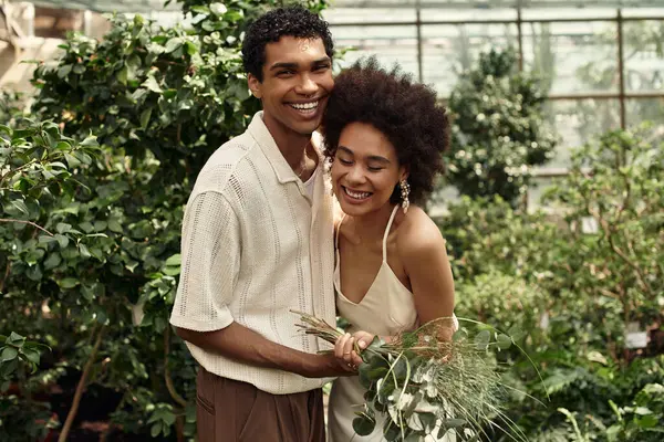 Genç bir çift sera atmosferindeki gelişmekte olan bitkiler arasında sıcak bir şekilde kucaklaşır..