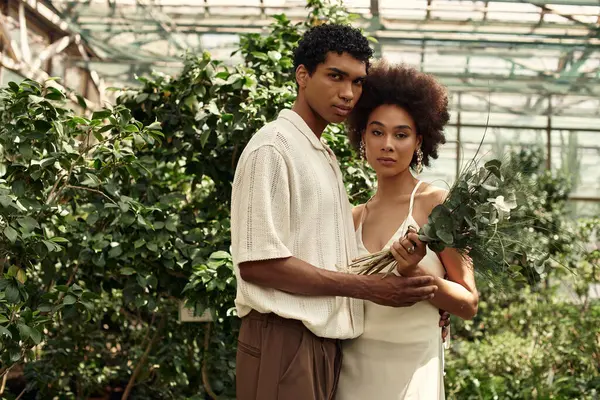 İki genç insan, sakin bir serada yemyeşil bitkilerle çevrili hassas bir anı paylaşıyor..