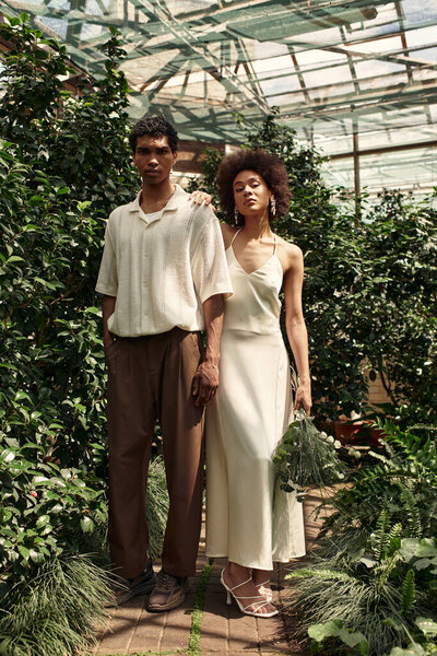 A joyful couple stands hand in hand in a greenhouse surrounded by vibrant plants and greenery.