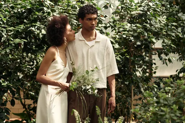 Genç çift, gelişen bitkilerle dolu canlı bir serada hassas bir anı paylaşıyor..