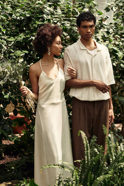 A young couple embraces lovingly surrounded by vibrant plants in a serene greenhouse atmosphere.