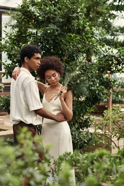 Huzurlu bir serada, genç bir çift canlı bitkiler arasında sarılır..