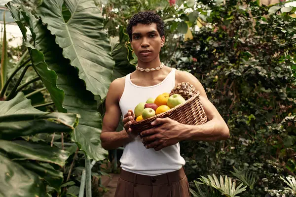 Genç ve şık bir adam canlı bir serada etkin poz veriyor yemyeşil bitkilerle dolu..