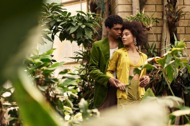 Genç bir çift, gelişen bitkilerle dolu canlı bir serada hassas bir anı paylaşıyor..