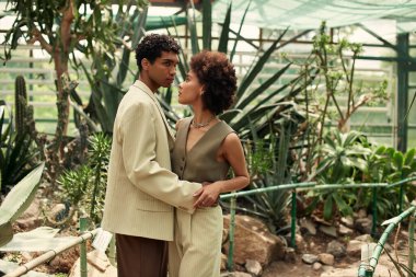 Bir çift, güzel bir serada çeşitli bitkiler arasında şefkatle kucaklaşır..