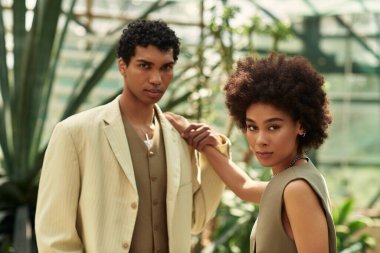 Genç bir kadın ve erkek, parlak bir serada yemyeşil bitkilerle çevrili hassas bir anı paylaşıyor..