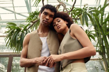 İki genç birey, serada canlı bitkiler ve dingin yeşillikler arasında sıcak bir şekilde kucaklaşıyor..