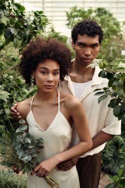 Canlı bir serada, genç bir çift gelişen yeşilliklerle çevrili hassas bir anı paylaşıyor..