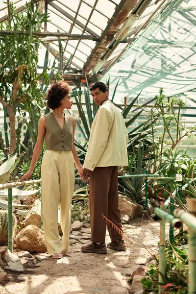 Sevgi dolu bir çift, sera atmosferindeki canlı bitkilerle el ele durur..