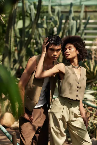 Bir çift canlı bir serada birbirine yakın duruyor, yemyeşil bitkilerle çevrili, sevgi saçıyor..