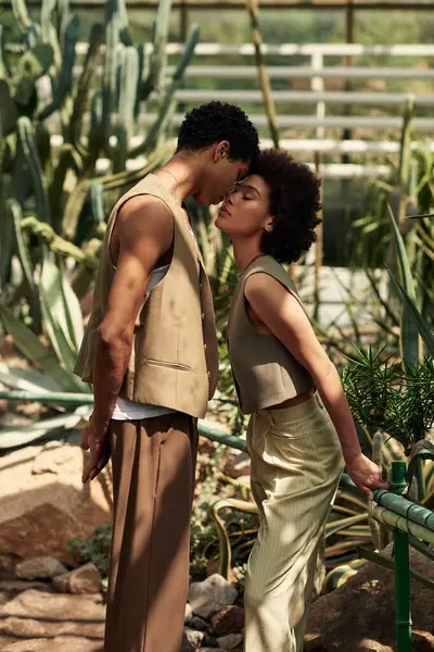 Güneşli bir serada kucaklaşan genç bir çift, canlı bitkilerin arasında aşklarını ifade eder..