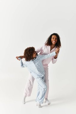 Uyumlu pijamalar içinde dans eden mutlu siyah anne ve kız. Gri arkaplan.