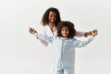 Mutlu siyah anne ve kızı pijamalarını giymiş, kollarını açmış, gri bir geçmişi var..