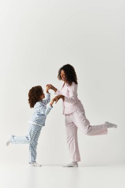 Mutlu bir Afro-Amerikan anne ve kızı pijamalarıyla bir bacağının üzerinde dengeli bir anı paylaşıyor..