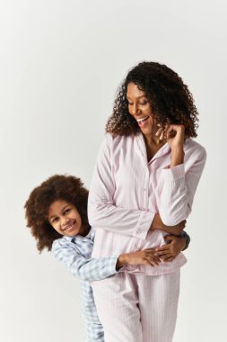 Siyah çocuk annesine sarılıyor, ikisi de aynı pijamaları giyiyor.