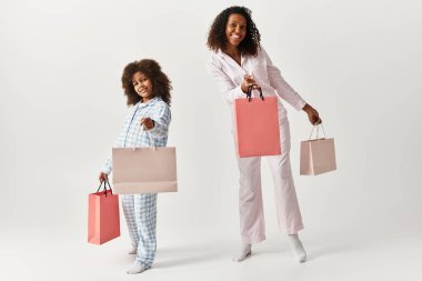 Siyah anne ve kızı aynı pijamalar içinde, alışveriş torbaları, gri stüdyo..