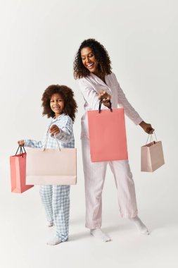 Afrika kökenli Amerikalı anne ve kız, eşleşen pijamalar içinde, alışveriş torbalarıyla bir stüdyoda poz veriyorlar..