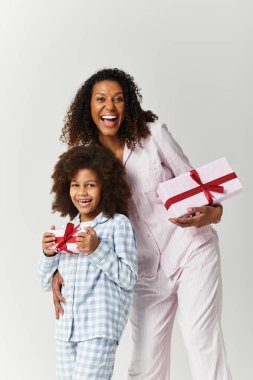 Siyah anne ve kızı pijamalarıyla gülümsüyor ve hediyeler tutuyorlar..