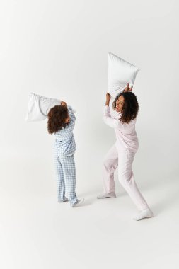 Siyah anne ve kızı gri pijamalarıyla yastık savaşı yapıyorlar..