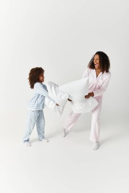 Siyah anne ve kızı birbirlerine uyumlu pijamalarıyla yastık savaşı yapıyorlar..