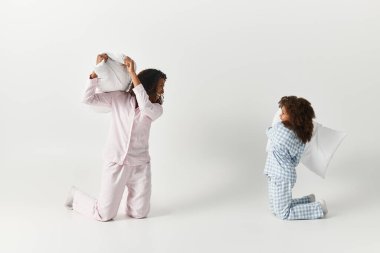 Siyah anne ve kız yastık savaşı. Pijamalarıyla yastık savaşı yapıyorlar.