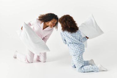 Siyah anne ve kız yastık eşleşen pijamalar içinde kavga ediyorlar..