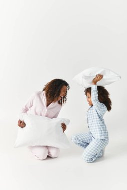 Pijama giymiş Afrikalı bir anne ve kız yastık savaşı yapıyorlar..