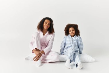 Neşeli bir Afrikalı Amerikalı anne ve kız aynı pijamaları giyerek birlikte oturuyorlar..