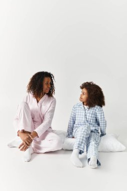 Parlak bir stüdyoda aynı pijamaları giyen siyah bir anne ve kız..