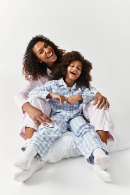 Aynı pijamaları giyen siyahi anne ve kız stüdyoda sarılıp gülüyorlar.