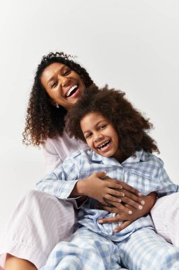 Afrika kökenli Amerikalı bir anne kızını tutuyor, aynı pijamaları giyiyor ve stüdyoda gülüyor..