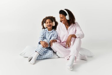 Aynı pijamaları giyen Afro-Amerikan anne ve kızı oturup kulaklıklarla müziğin tadını çıkarıyor..