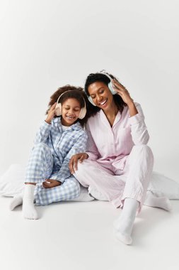 Uyumlu pijama giyen siyah anne ve kız kulaklıkla müzik dinliyor..