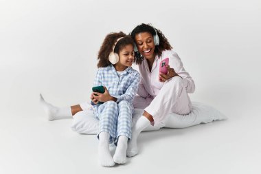 Aynı pijamaları giyen siyah anne ve kız, kahkahaları paylaşıyorlar ve parlak stüdyoda telefona bakıyorlar..