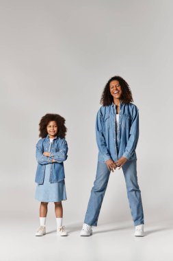 Neşeli bir Afro-Amerikan anne ve kızı eşleşen kot giysiler içinde poz veriyorlar..