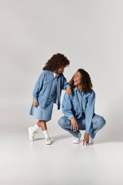 Afrika kökenli Amerikalı anne ve kız, gri bir zemine karşı uyumlu kot kıyafetlerle kaynaşıyor..