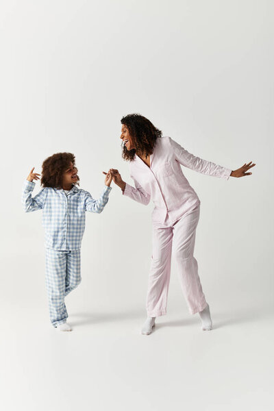 Happy Black mother and daughter in pajamas dance in studio.
