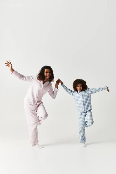 An African American mother and daughter joyfully dance wearing matching pyjamas.