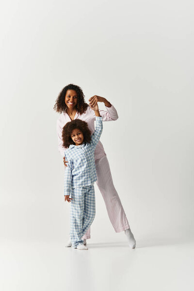 Black mother and daughter in matching PJs, holding hands on grey background.