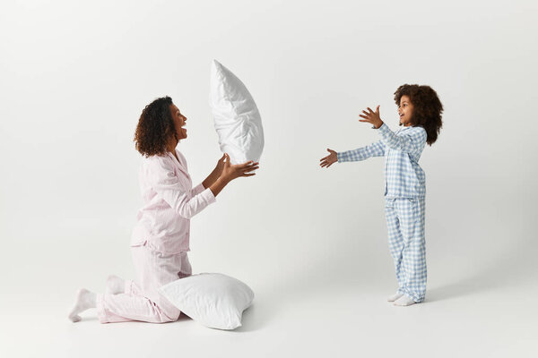 In a studio setting, an African American Mother and daughter play with pillows.