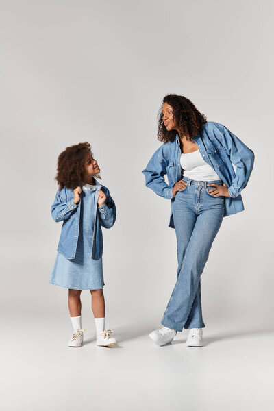 African American Mother and Daughter, both in denim, posing on grey background.